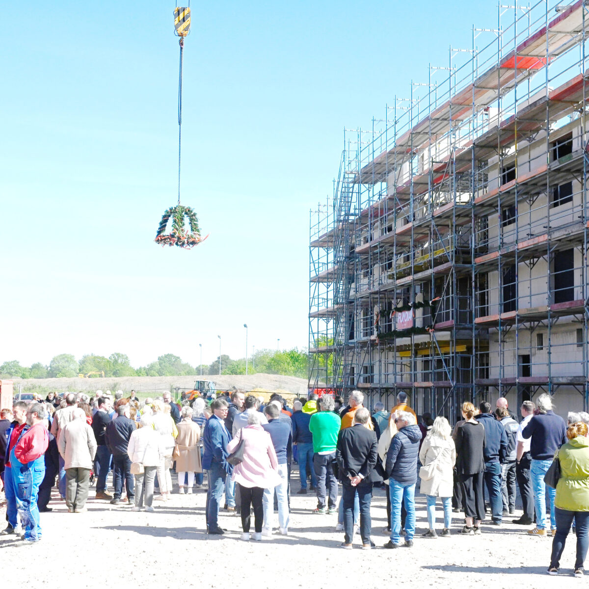 Während Ober-Polier Paul Miller vom Gerüst des Rohbaus von Haus Thomas mit seinen Polieren Mahmut und Saban Jasarevic den Richtspruch vorträgt, schauen rund 150 Gäste zwischen den beiden Häusern zu, wie der Richtkranz vom Krahn hochgezogen wird.